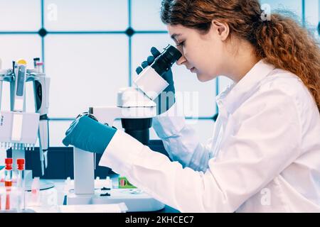young adult female student working with a microscope examining biological samples using a microscope in a genetic laboratory Stock Photo