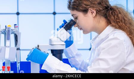 young adult female student working with a microscope examining biological samples using a microscope in a genetic laboratory Stock Photo