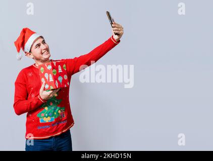 Christmas handsome man taking a selfie holding a gift isolated. Happy guy taking a christmas selfie isolated, Smiling young man in christmas hat holdi Stock Photo