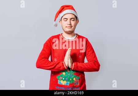 Guy with hands together praying in christmas isolated, concept of person with christmas hat praying and making a wish. Man with christmas hat with pra Stock Photo