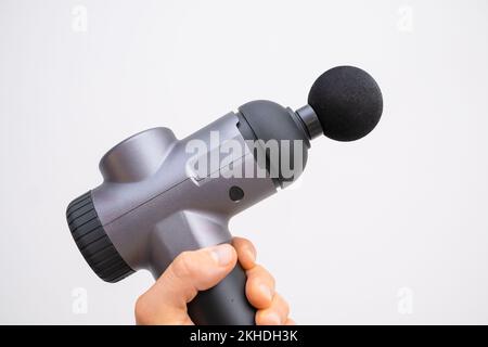 Electric massager gun in mans hand on the white background. Recovery after a workout. Stock Photo