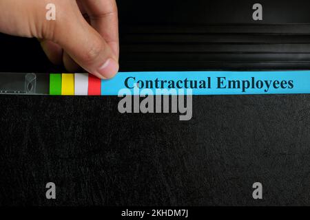 Hand picking contractual employees file record in black binder folder. Human resources concept. Stock Photo