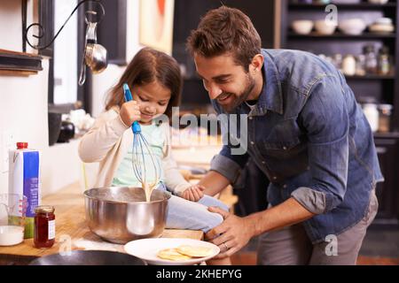 Youre doing great sweetheart. A cute little girl helping her dad make pancakes at home. Stock Photo