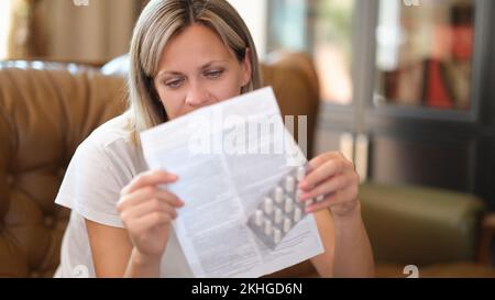 Woman sitting on sofa and reading instructions for medical use of pills Stock Photo