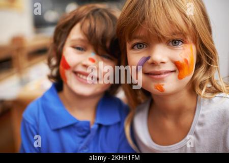 Being an artist is messy business. A portrait of two cute young siblings with faces full of paint. Stock Photo