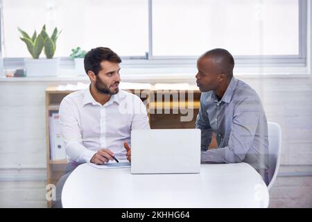 Finding solutions as a team. Two businessmen sitting in an office with a laptop while having a meeting. Stock Photo
