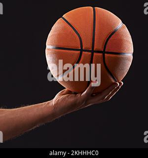 Dont drop the ball. Cropped image of a mans hand holding a basketball against a black background. Stock Photo