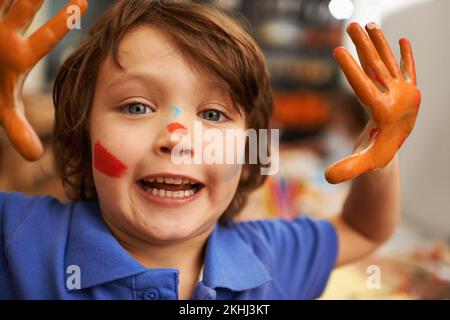 Art class mischief. Cute little boy showing his hands and paint covered face. Stock Photo