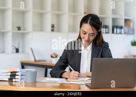 Asian accountant using calculator while taking notes on office desk. Stock Photo