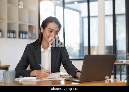 Asian accountant using calculator while taking notes on office desk. Stock Photo