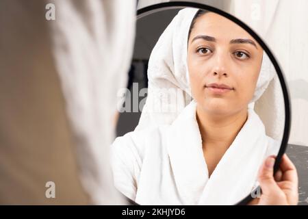 Beautiful woman looking mirror after shower her hair wrapped in towel. Morning care concept idea. Personal hygiene, cosmetics treatment procedures. Stock Photo