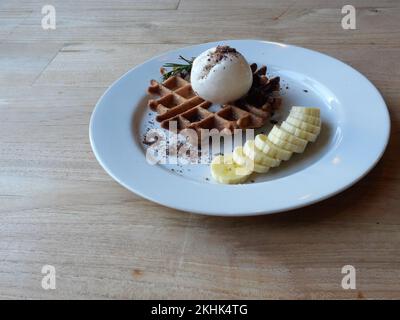 Ice cream on waffle and cocoa powder and banana slice on a white plate on brown wood table Stock Photo