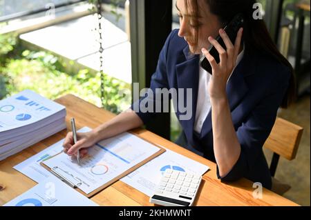 Professional and confident millennial Asian businesswoman talking on the phone with her business client while working at her desk. top view Stock Photo