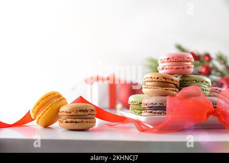 Heap of French macaroons of various flavors with red bow and gift on white isolated background. Front view. Stock Photo