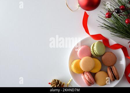 Plate of French macaroons of various flavors on a plate on a white table with Christmas decorations. Top view. Stock Photo