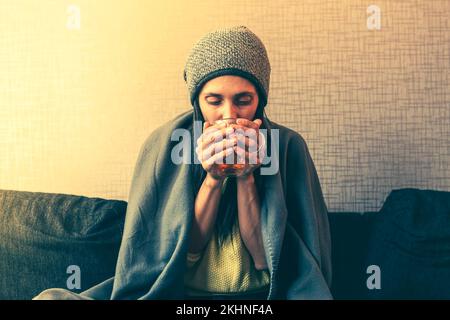 Caucasian Worried sad woman sits under blanket on sofa with cup of tea, Rising costs in private households for gas bill due to inflation and war, Ener Stock Photo