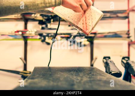 Ski repair shop employee workman melts drops red wax on snowboard with special wax iron. Ski snowboard waxing service and preparation Stock Photo