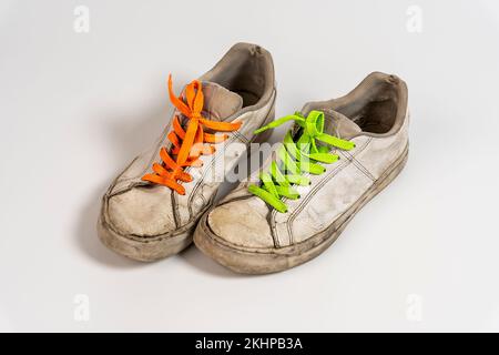 worn old torn white sneakers with colored laces on a white background Stock Photo