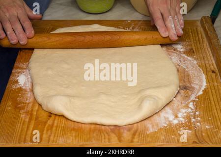 Rolling Out Dough For Pizza. With a Wooden Rolling Pin, Roll Out the Dough as Thin as Possible Stock Photo