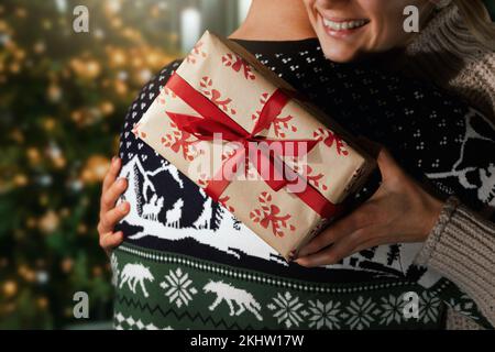 woman embrace her husband next to the christmas tree after receiving a gift box at home Stock Photo