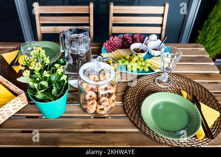 Outdoor table with taralli and flower plant as a delicious plate with salami and cheese lies on the side. Dish with pepperoni, cheese and green grape Stock Photo