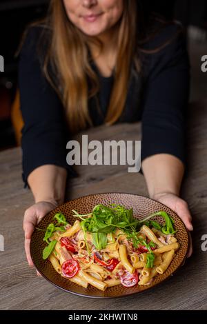 Vertical cropped woman in black outfit holding juicy, ready to eat, fresh organic pasta with basil, sauce, meat, tomato Stock Photo