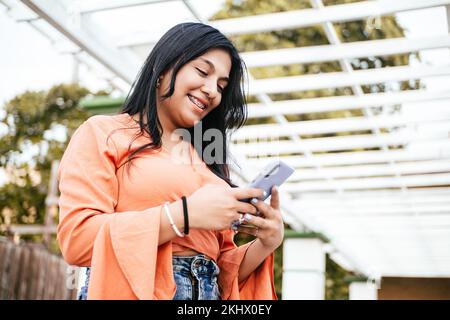 A smiling Latin female using a mobile phone outdoors Stock Photo