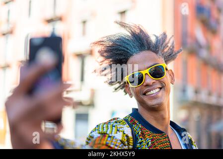 afro american stilish man looking at the smartphone, influencer creating contents for social media, selfie time of a weird haired african guy Stock Photo