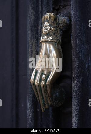 Closeup view of elegant vintage brass door knocker in shape of hand holding ball isolated on ancient dark brown wooden door, Montpellier, France Stock Photo