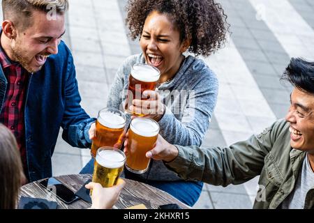 young people group toasting with pints of beer, generation z men and women having fun, focus on drink glasses Stock Photo