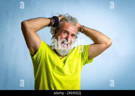 Hipster bearded man looking at the camera with worried and painful expression, adult male putting his hands in his hair to despair, studio shot with y Stock Photo