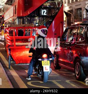 Traffic on Regent Street during the festive season with a learner motorcyclist wearing a Santa Claus hat. London. Stock Photo