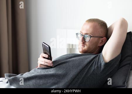 Man laying on a couch with mobile phone. Relaxing at home. Stock Photo
