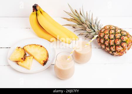 Banana and pineapple smoothie on white wooden table with ingredients. Detox diet concept, summer vitamin drink. Top view Stock Photo
