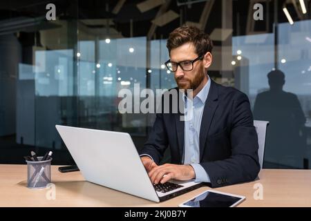 Serious businessman working inside office at work, mature boss in business suit sitting at computer and table, senior man thinking. Stock Photo