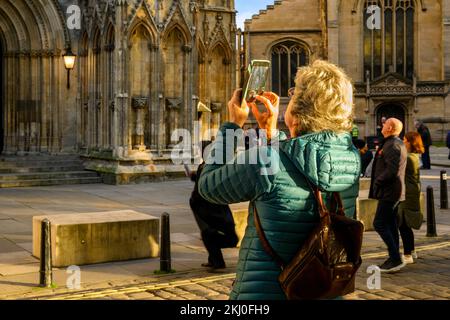 Person using mobile phone camera (shot of new Elizabeth 2 statue on niche & visitors standing) - York Minster west front, North Yorkshire, England UK. Stock Photo