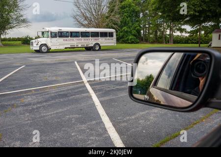 Photographer takes a picture of a white American church bus from his car in a parking lot Stock Photo