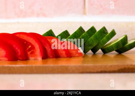 Freshly cut tomatoes and sliced ​​cucumbers on white background pink wall. Stock Photo