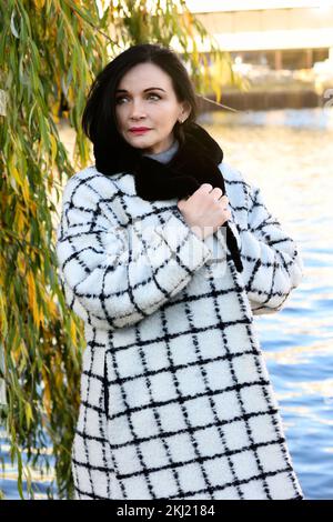 beautiful woman in coat walking along a river in the city Stock Photo