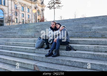 two women sitting outdoors on steps and hugging Stock Photo
