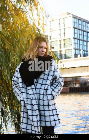young woman in a coat walking along a river in the city Stock Photo