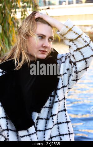 young woman in a coat walking along a river in the city Stock Photo