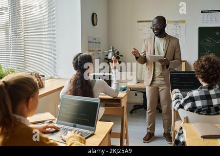 African American teacher using tablet pc to teach children information technology at class Stock Photo