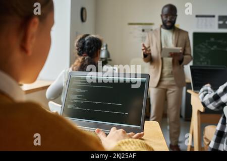 Girl examining computer program on computer at desk at lesson with teacher standing in background Stock Photo