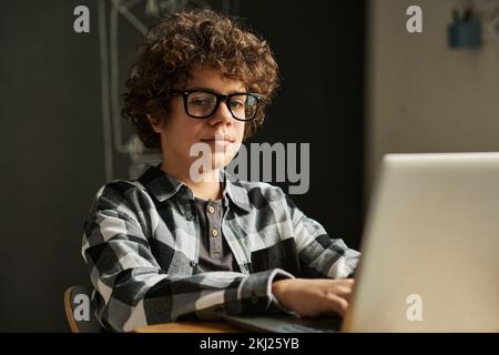 Portrait of schoolboy in eyeglasses looking at camera using laptop sitting at desk during lesson Stock Photo