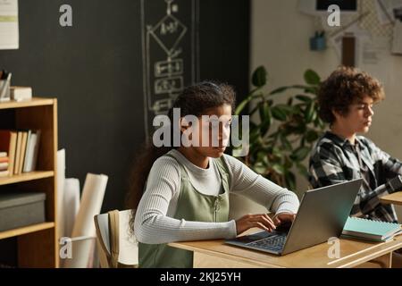 African American girl typing on laptop while sitting at her desk at lesson with her classmates Stock Photo