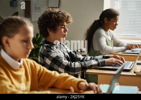 Group of children sitting at desks and using computers at their study at lesson Stock Photo