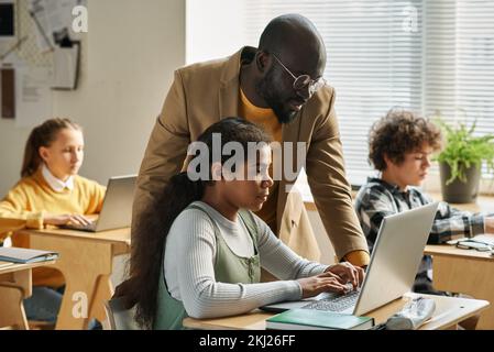 African American teacher teaching children of basics of using computer during lesson at class Stock Photo