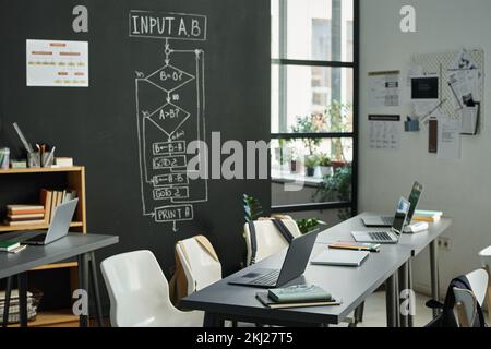 Modern classroom with computers on table for studying IT technology with blackboard with charts in background Stock Photo