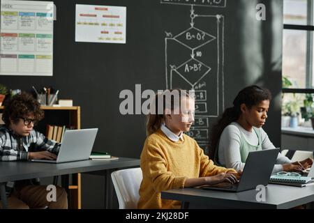 School children studying at IT class, they sitting at table and typing on computers, they learning to work with new computer program Stock Photo